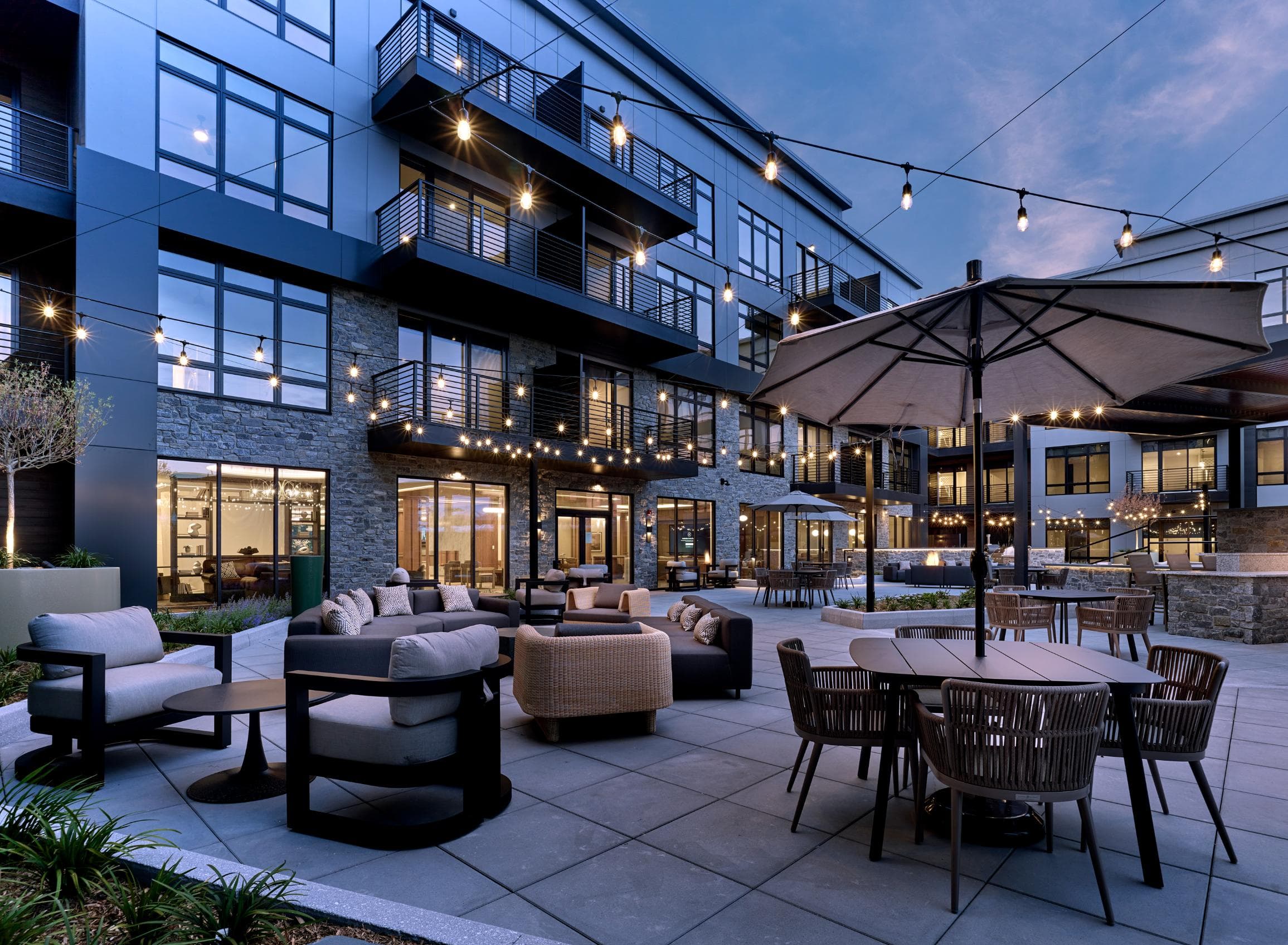 A patio area with tables and chairs is lit up with string lights.
