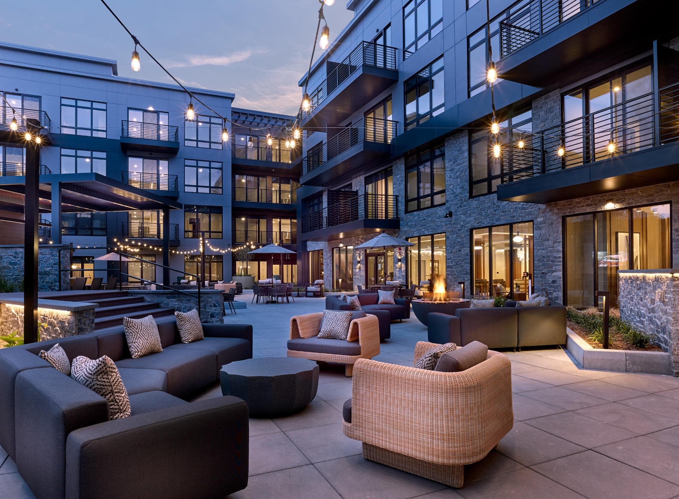 A patio area with couches and tables is illuminated by string lights.